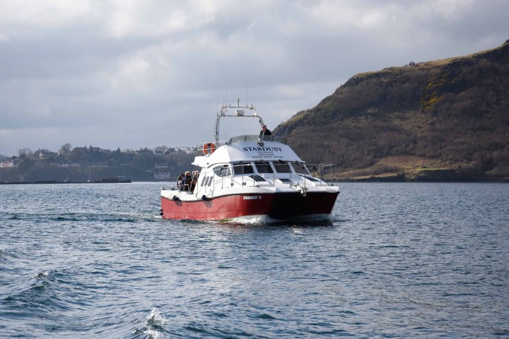 Boat named Stardust on a lake with hills in the background under cloudy skies.