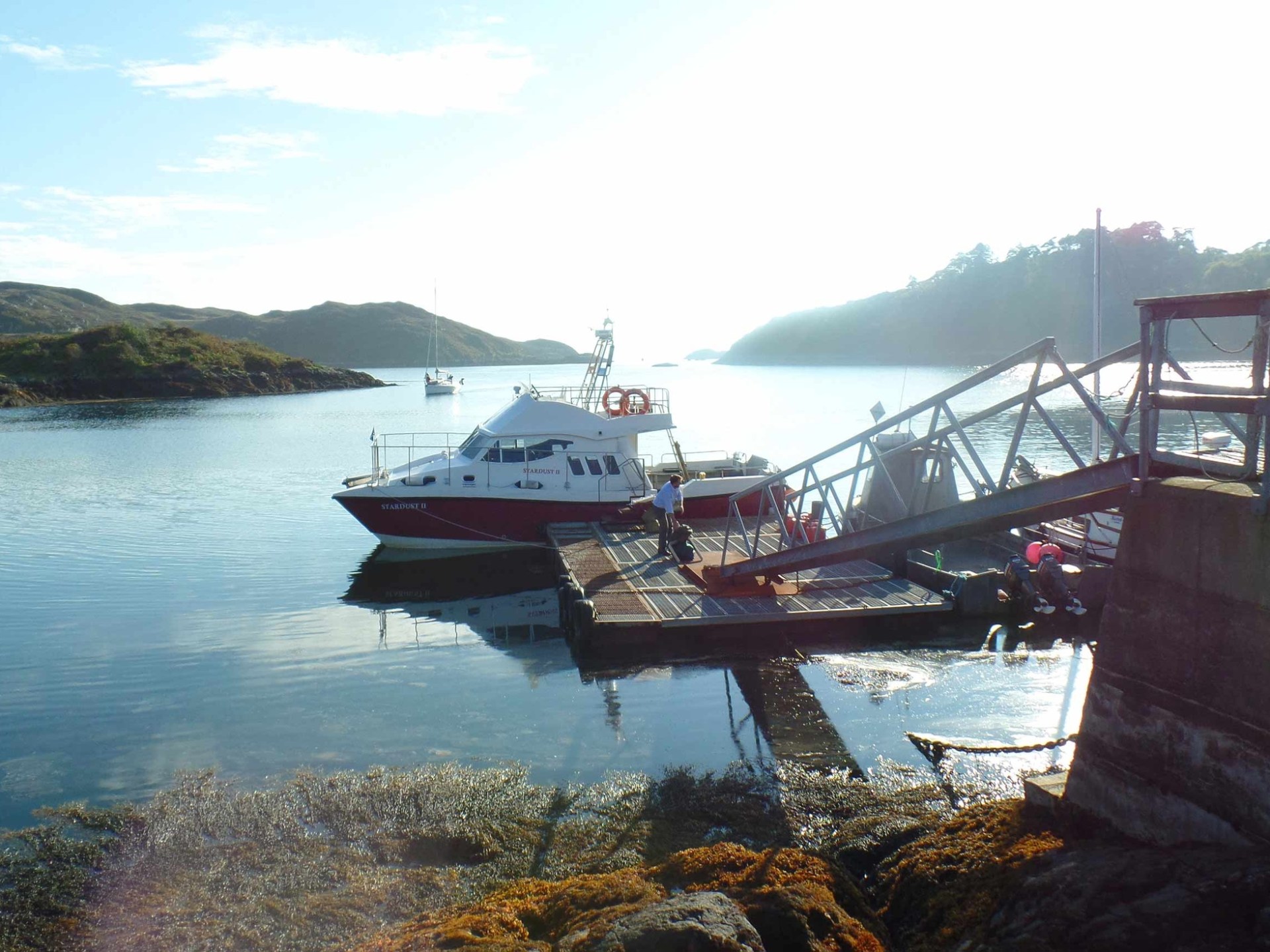 Boat docked at a pier on a serene lake with distant hills and clear sky.