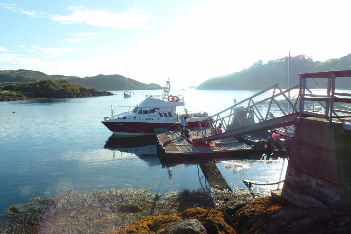 Boat docked at a pier on a serene lake with distant hills and clear sky.