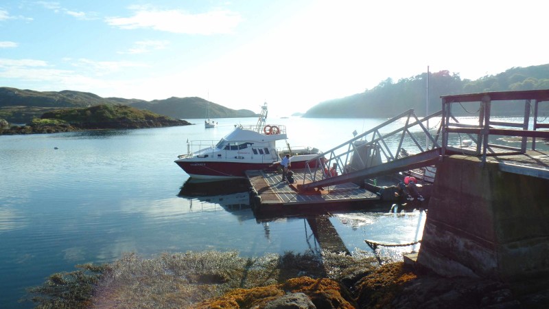 Boat docked at a pier on a serene lake with distant hills and clear sky.