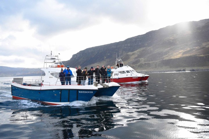 Two boats with people on a lake, mountain in background, cloudy sky.